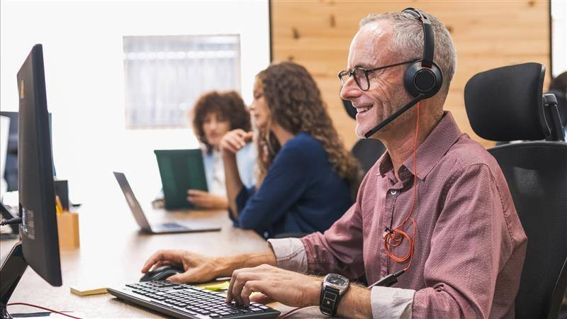 Mature_Businessman_Using_Computer_And_Headset_In_Coworking_Office_original_2948546