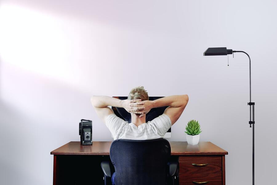 A remote worker kicks back at his desk, hands on head, awaiting instructions from his boss.